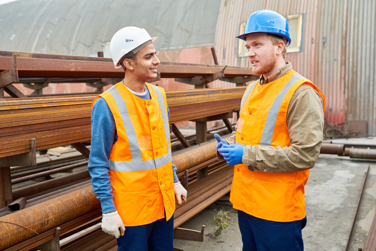 Two workers in uniform chat during break outside of modern metalworking plant